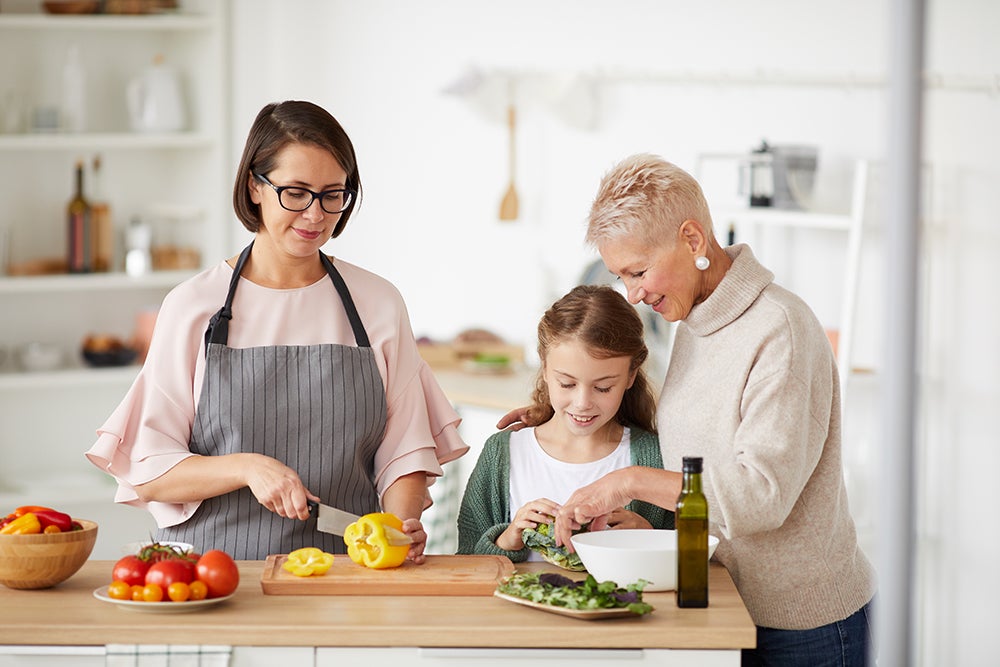 Family cooking dinner together Young mother and grandmother teaching little girl to prepare vegetable salad in the kitchen at home